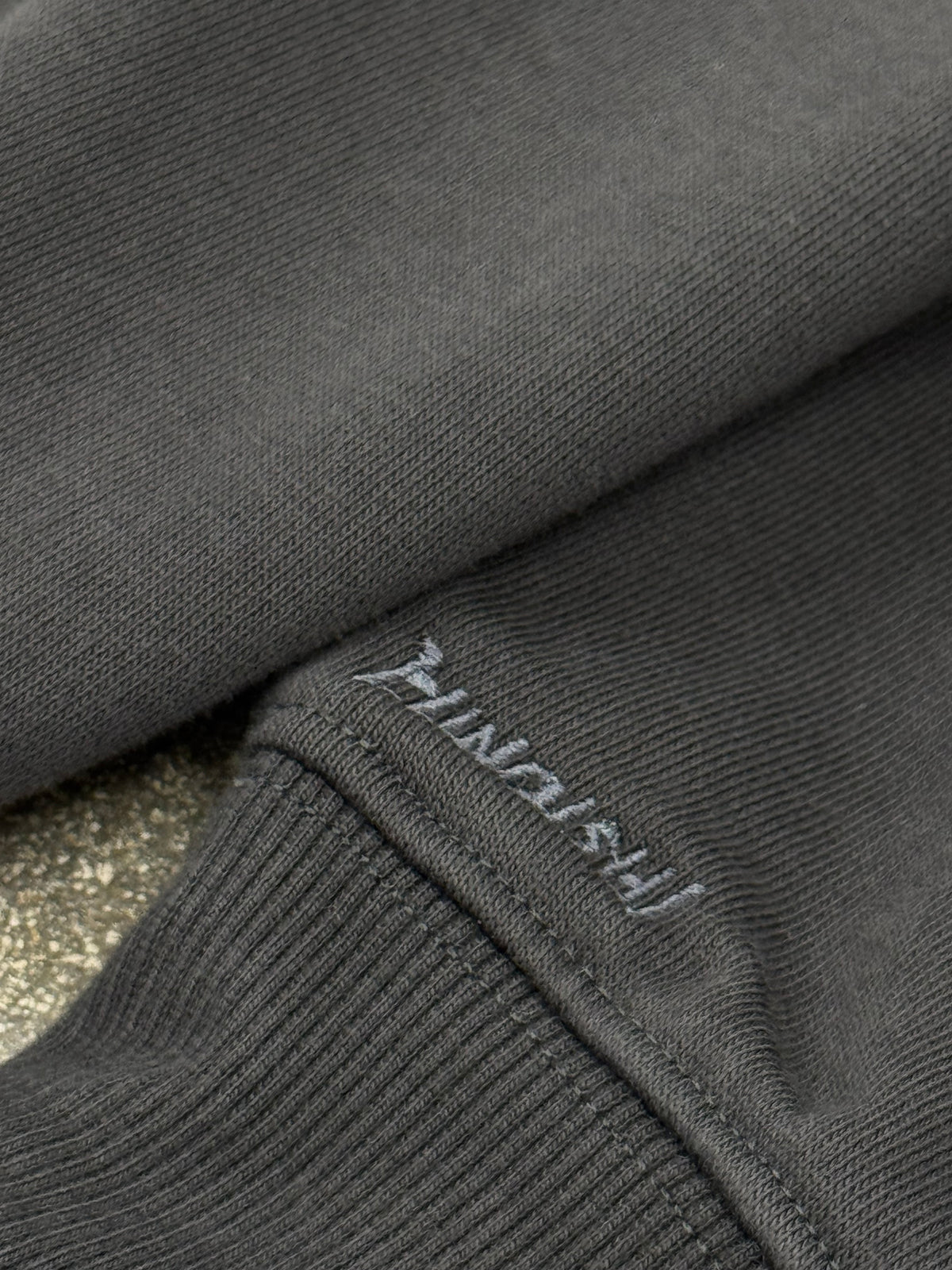 Close-up of the embroidered HINOISHI logo near the cuff of the Kakashi vs Kakuzu hoodie