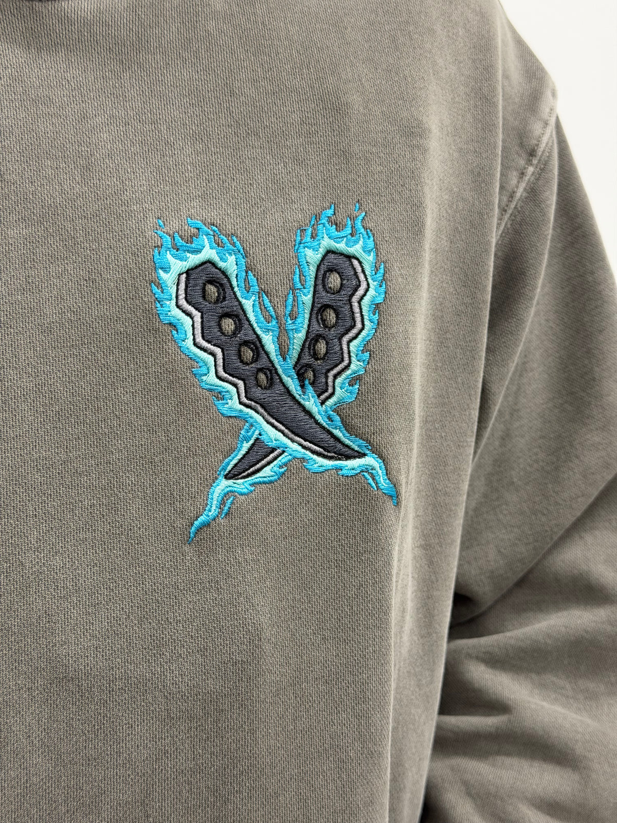 Close-up of chest embroidery: Asuma's crossed trench knives wrapped in blue flames
